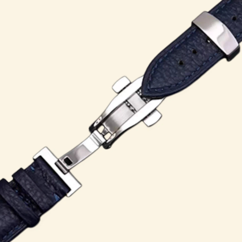Baroque silver Apple Watch case with navy blue leather strap — three-quarter product shot showing scrollwork bezel and silver cross emblem stud, cream background