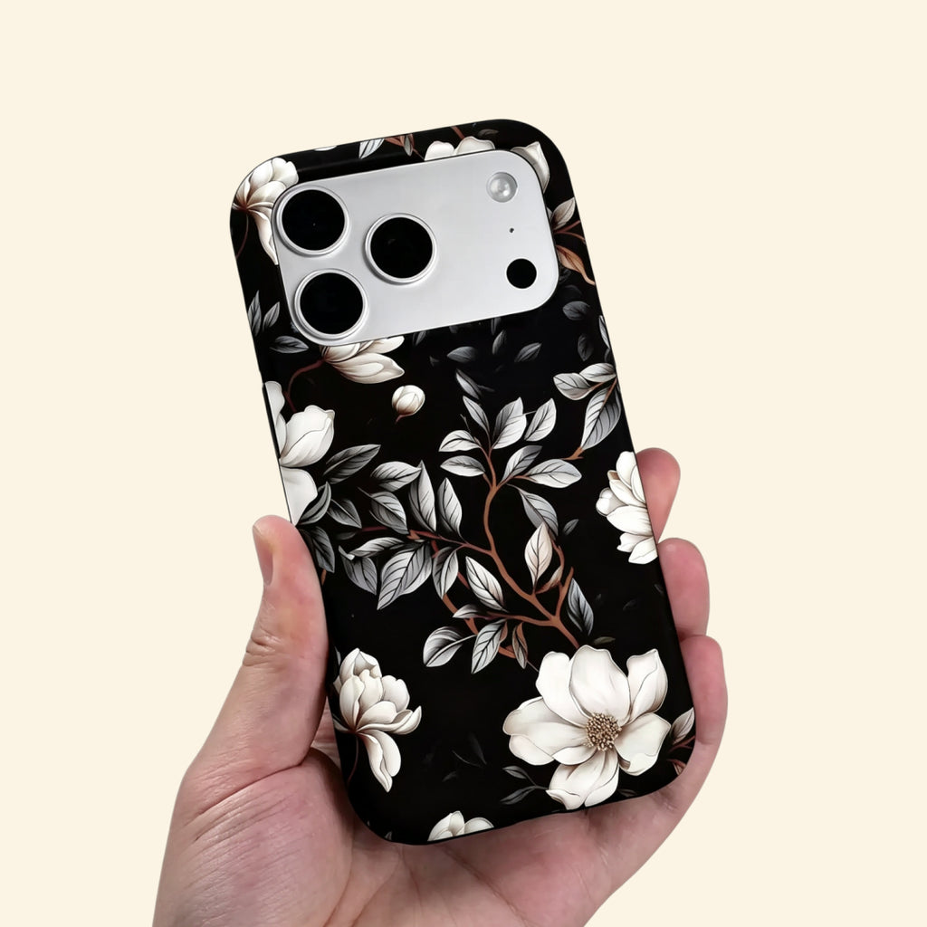 The Midnight Bloom case – hand-held lifestyle shot showing full ivory magnolia botanical artwork on matte black
