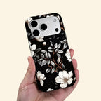 The Midnight Bloom case – hand-held lifestyle shot showing full ivory magnolia botanical artwork on matte black