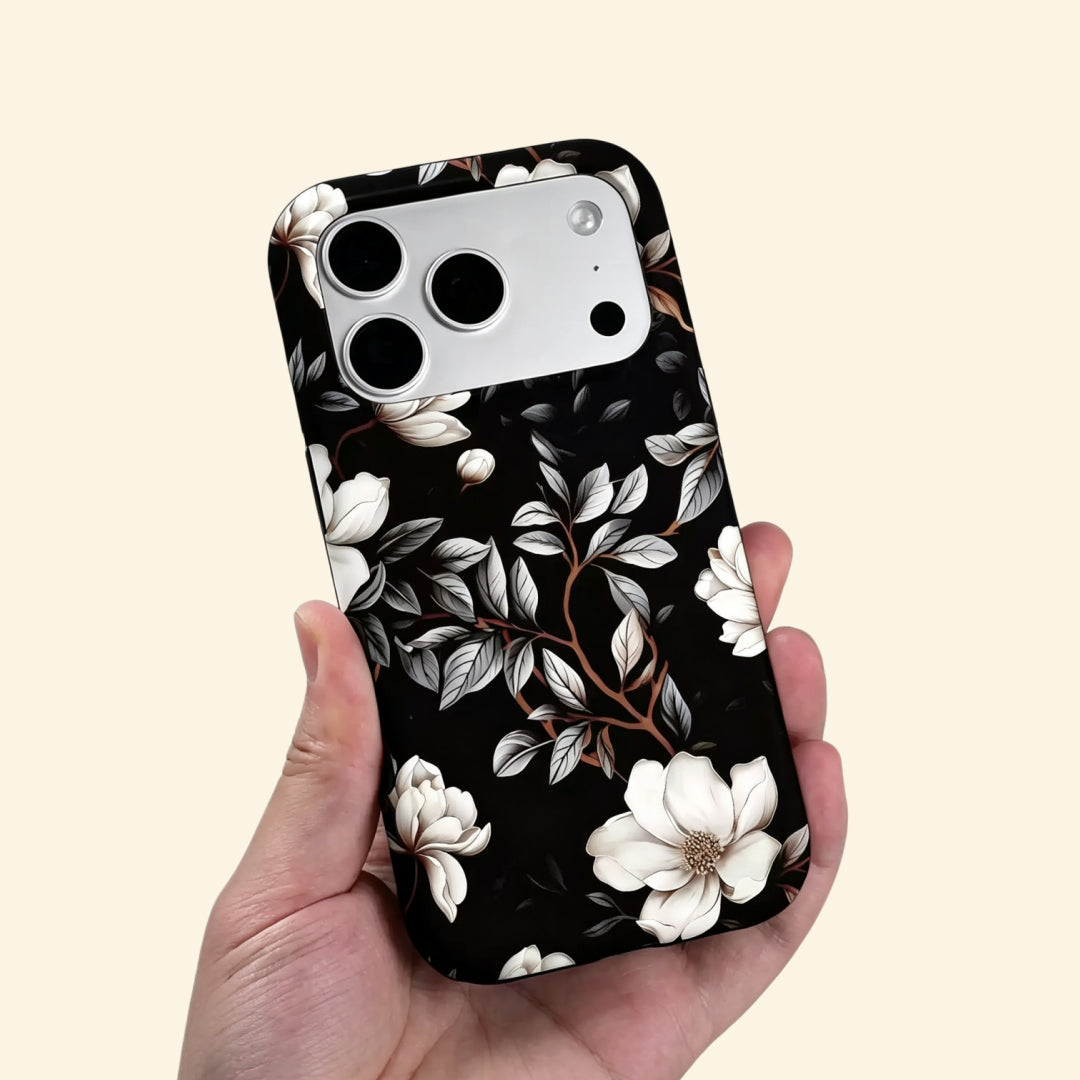 The Midnight Bloom case – hand-held lifestyle shot showing full ivory magnolia botanical artwork on matte black