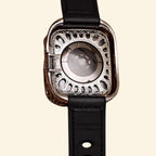 Baroque Archival Suite flat lay — silver engraved case with matte black leather hybrid strap and matte black pin buckle, diagonal angle