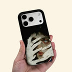 The Silent Gaze case – low-angle side view showing camera island and chalky pale hand detail with blue eye and crimson accents