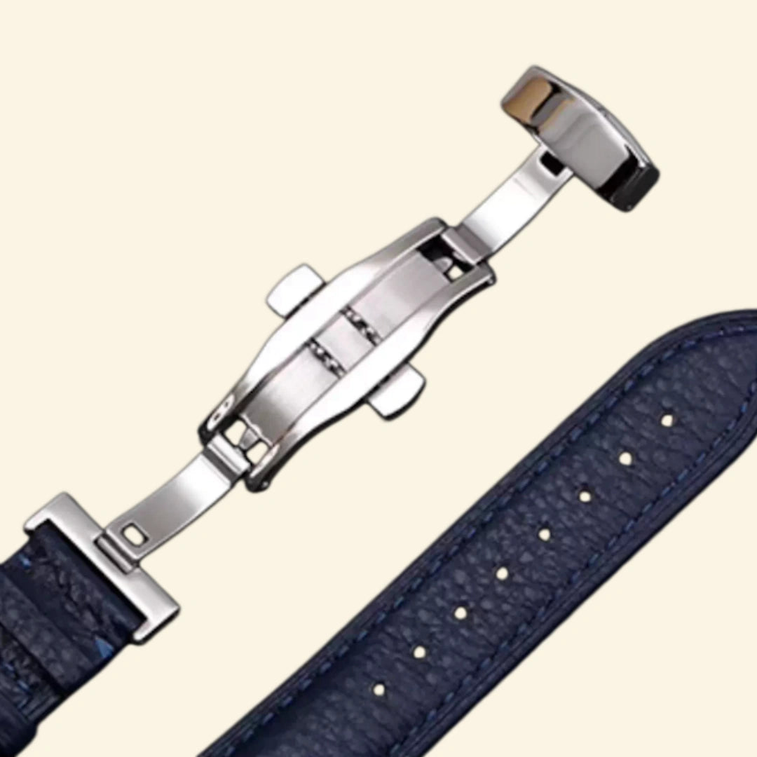 Navy blue pebble-grained leather Apple Watch strap — diagonal close-up showing stainless steel deployment clasp closed and strap taper, cream background